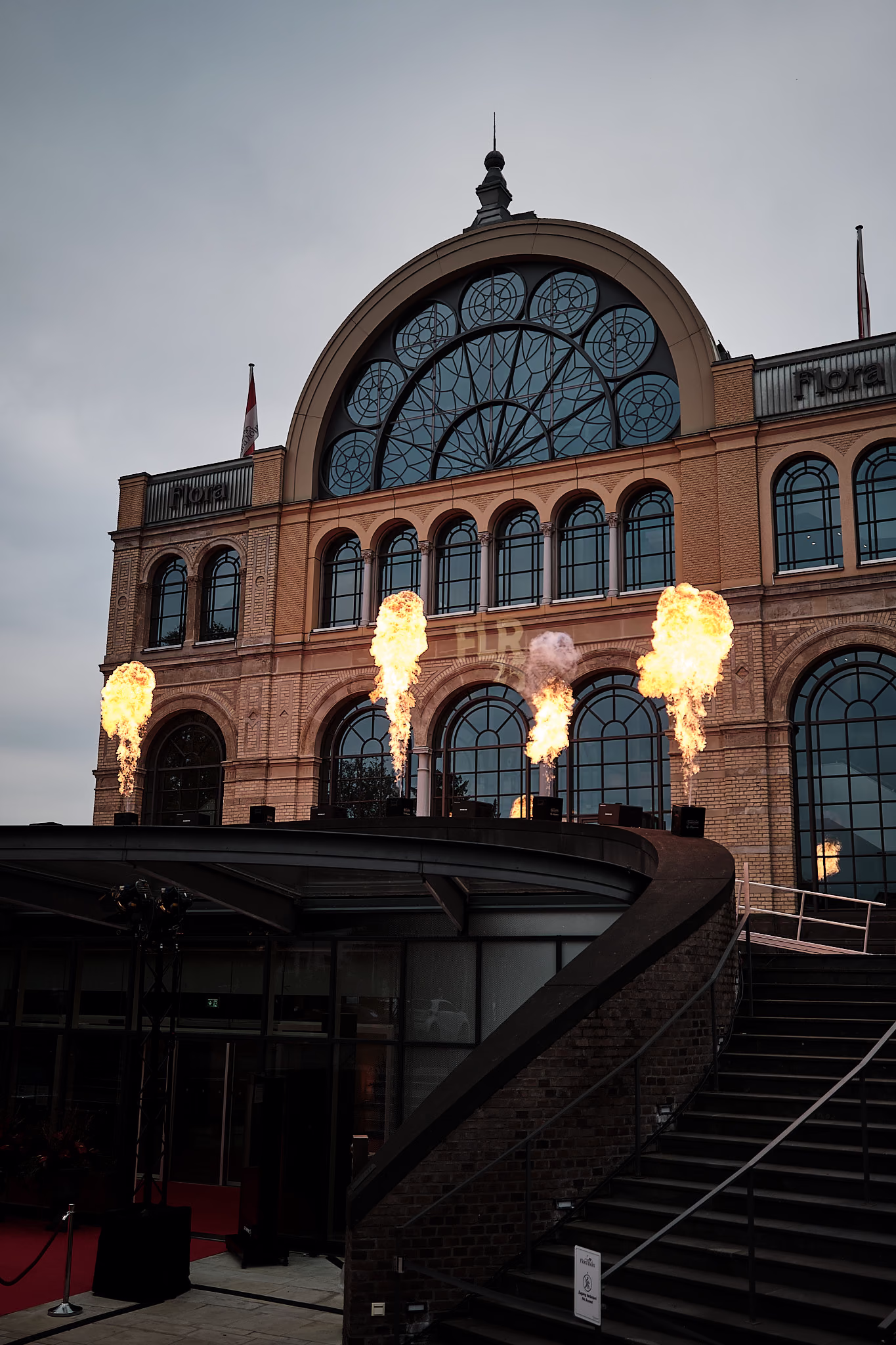 Die Fassade der Flora am Abend, davor schlagen Feuersäulen zur Begrüßung der Gäste